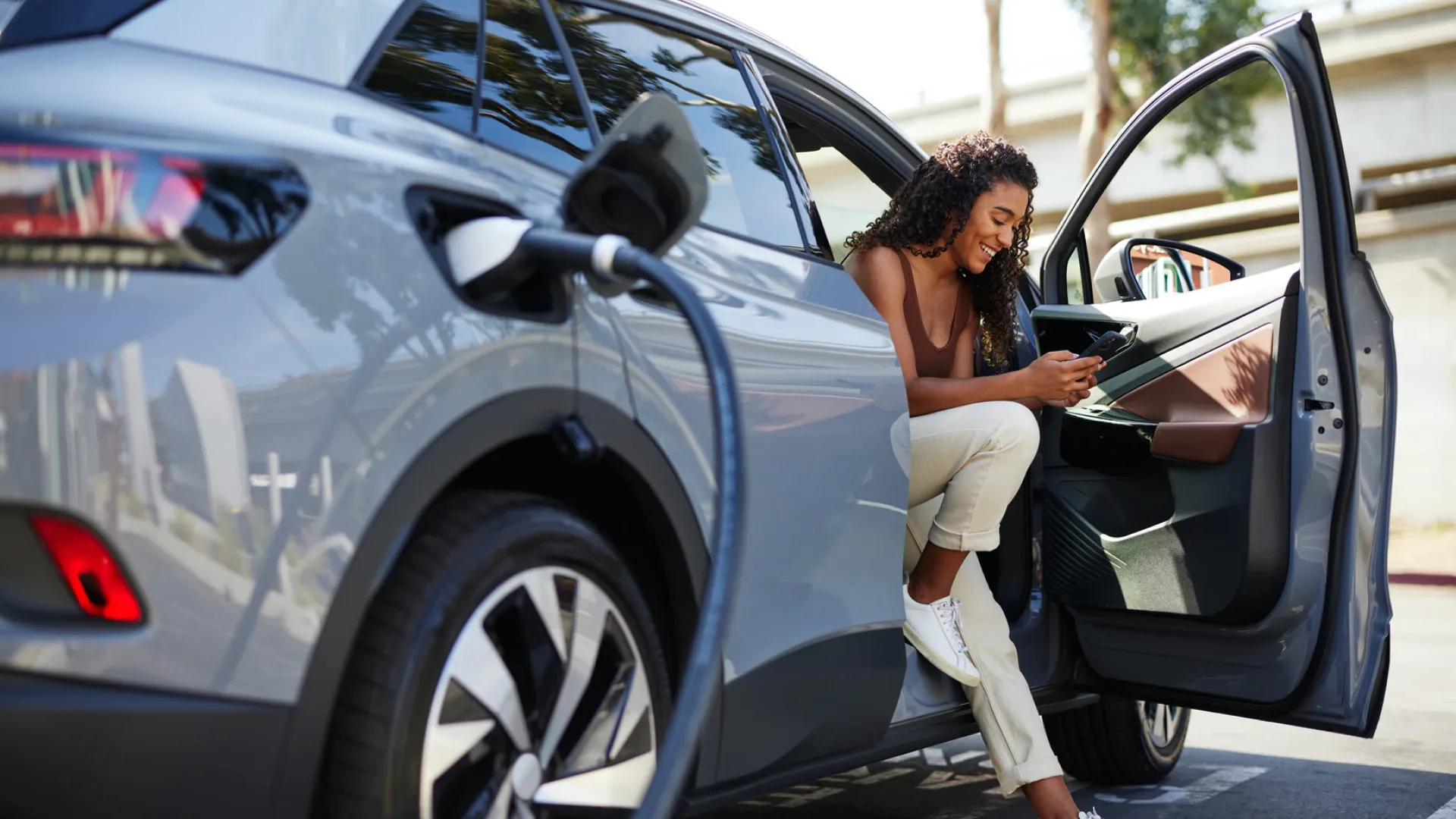 Women sat in car on her phone while her EV car chargers.